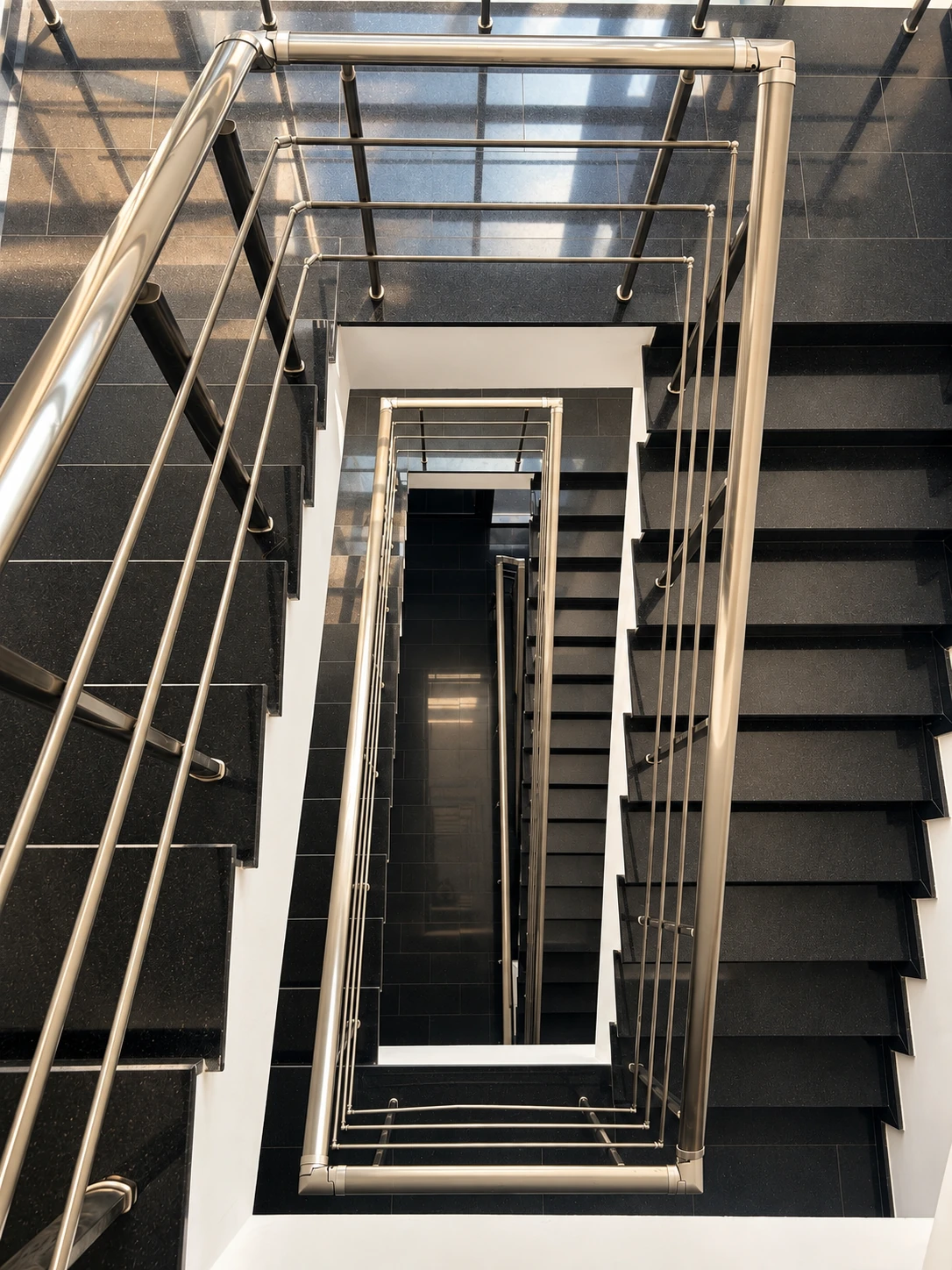 Architectural staircase seen from above, with black granite steps and brushed steel balustrades